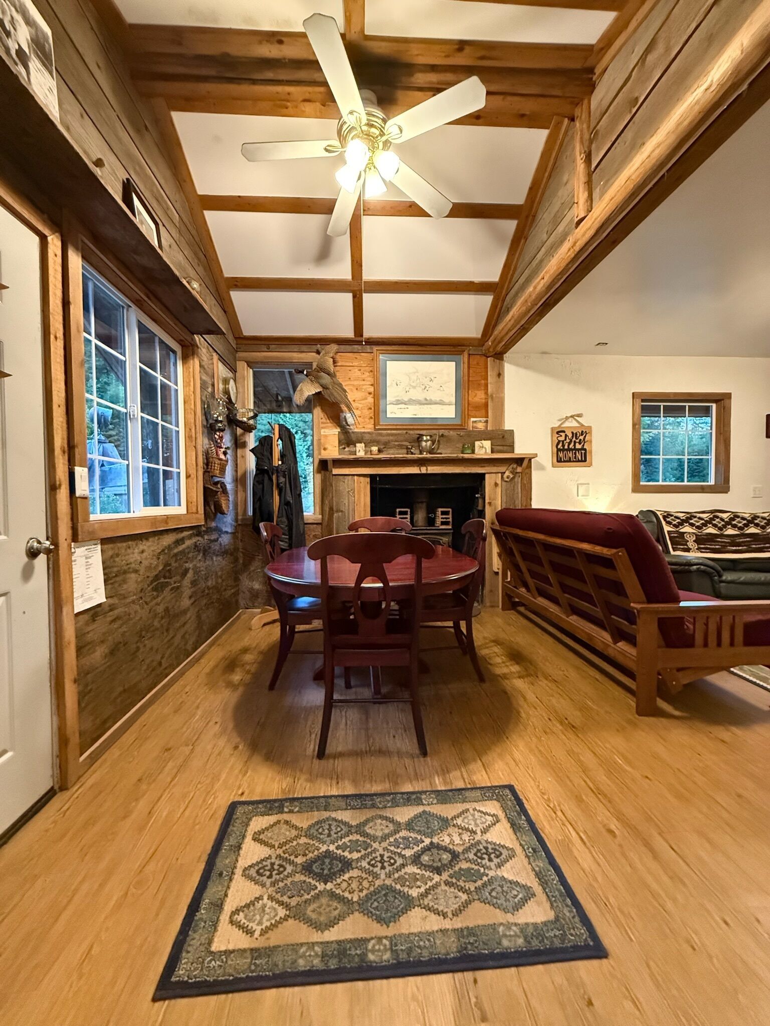 A wooden interior with a dining table, chairs, a fireplace, and a ceiling fan.