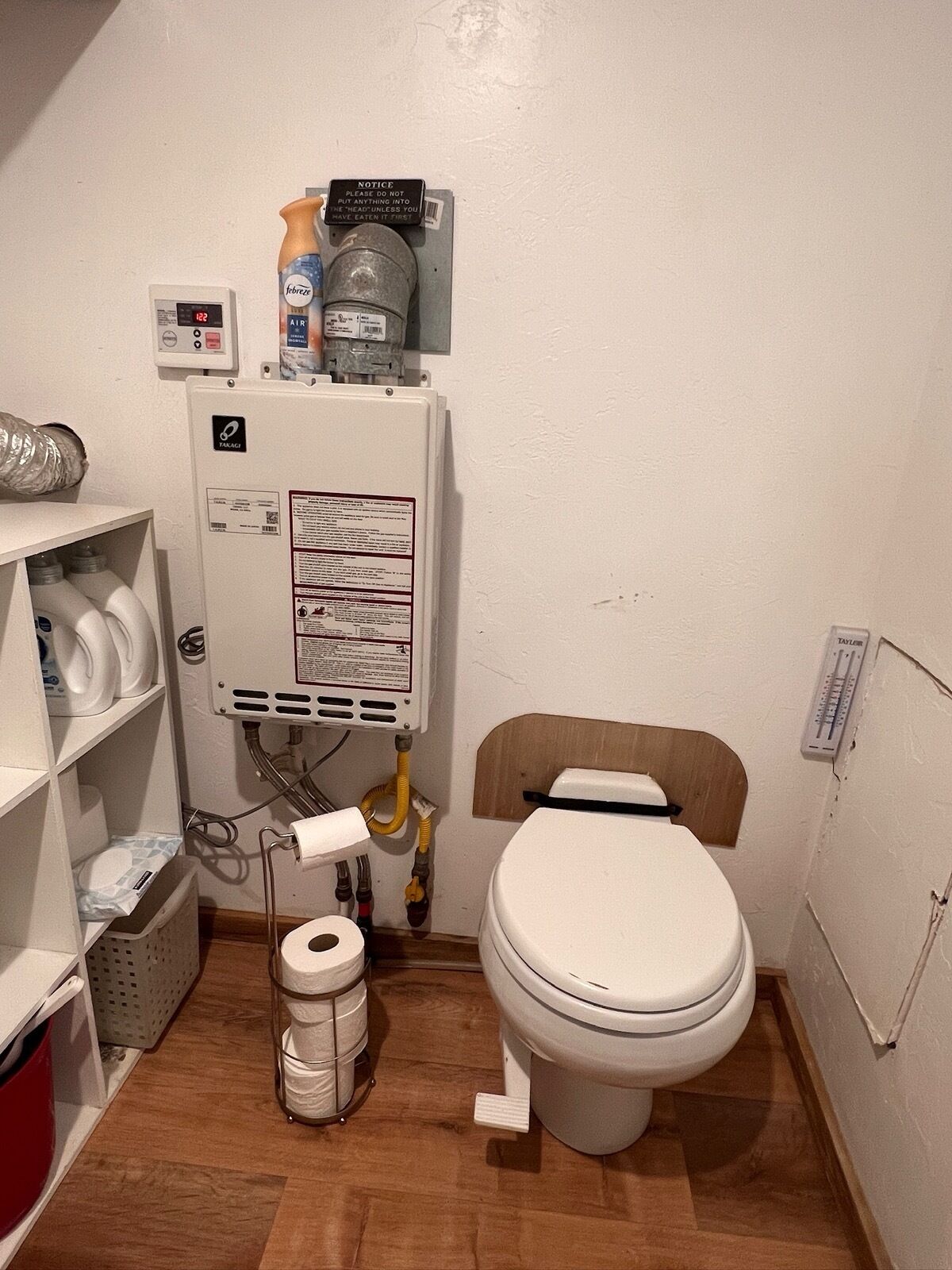 Pieni kylpyhuone, jossa on wc, lämminvesivaraaja ja hylly, jossa on hygieniatuotteita.