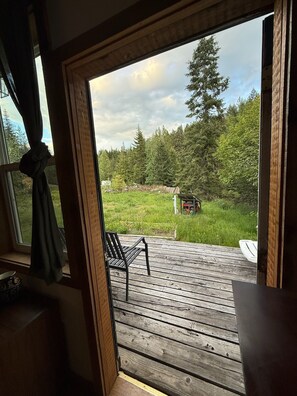 A wooden deck with a bench, a view of a forested area, and a small structure in the background.