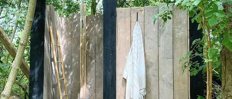 A wooden outdoor seating area with a bench, a ladder, and a hanging cloth.