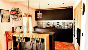 Een moderne keuken met een eethoek, met een houten tafel, stoelen, hanglampen en een spatwand met geometrische patronen.