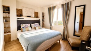 Een slaapkamer met een bed, een stoel, een boekenkast, een raam met gordijnen en een spiegel.