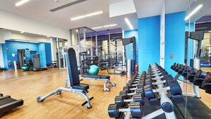 Un gimnasio con equipamiento de ejercicio, un espejo grande en la pared y piso de madera.