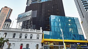 Un edificio alto con fachada de vidrio moderno, junto a un edificio histórico con puerta roja.