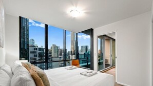 Una habitación de hotel moderna con una cama grande, vistas a la ciudad y una puerta corrediza a un balcón.