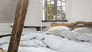 A room with a wooden beam, a window with a view of trees, a bed with white bedding, and a white lamp on a bedside table. - Friends in small fishing home Betty Fjord (Harpelunde)