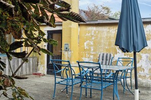 A patio with blue metal chairs and a table, a yellow wall, and a blue umbrella. - Friends in small fishing home Betty Fjord (Harpelunde)