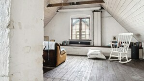 A loft-style room with a sloped ceiling, a window with a view, a rocking chair, a sofa, and a bookshelf. - Friends in small fishing home Betty Fjord (Harpelunde)