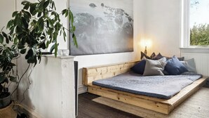 A room with a wooden platform bed, a large abstract painting, a potted plant, and a window with a view. - Friends in small fishing home Betty Fjord (Harpelunde)