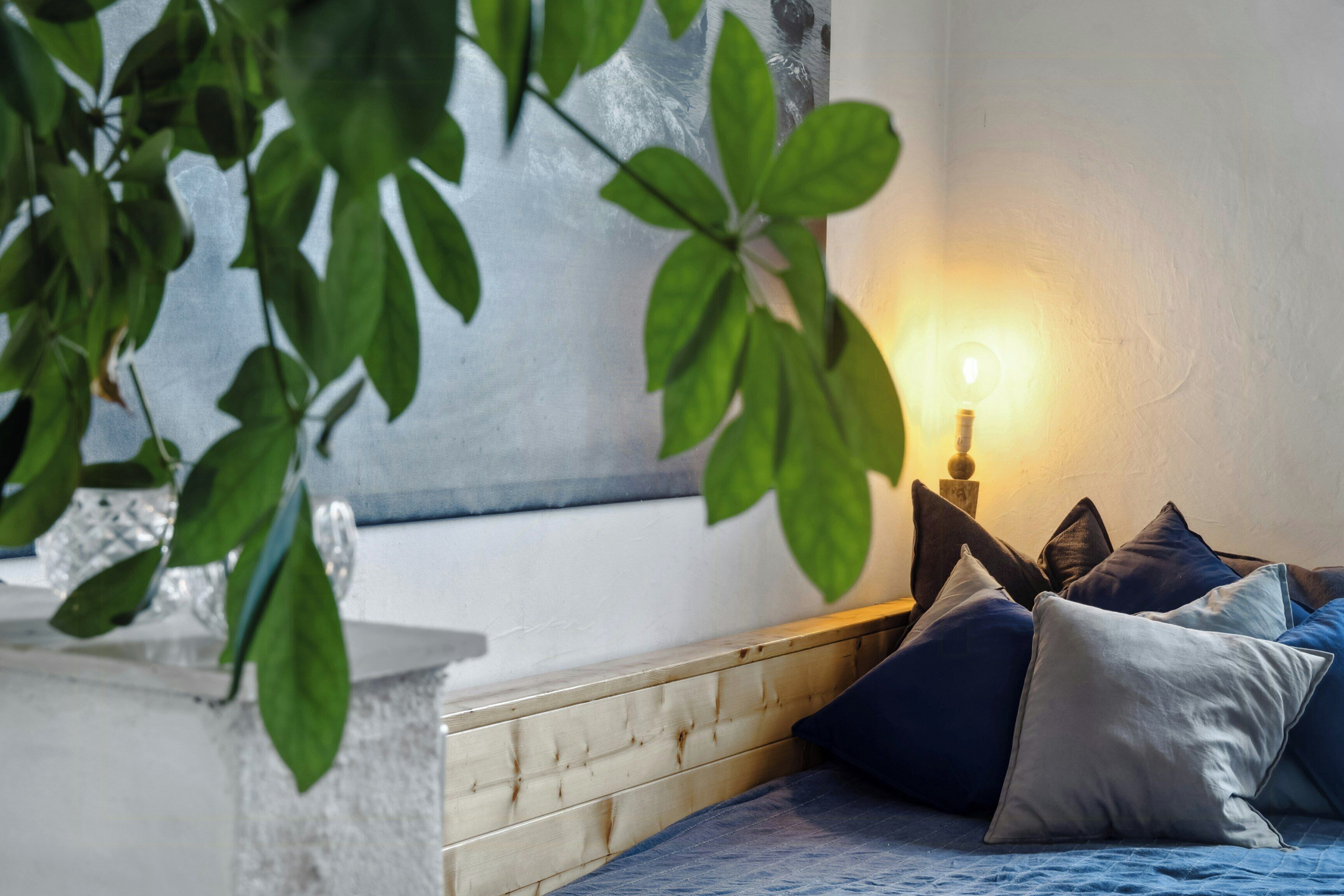 A bedroom with a bed, pillows, a bedside table, and a wall-mounted lamp.