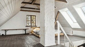 Een slaapkamer met zolderafwerking, schuine plafonds, houten balken, dakraam, een bed en een bankje.