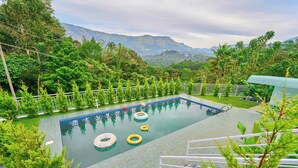 Piscina con vista a montañas, rodeada de vegetación y una cerca blanca.