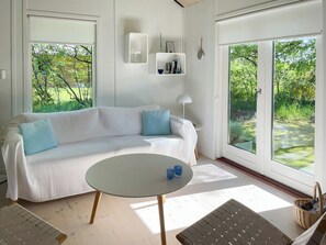 Un salón moderno con un sofá blanco, una mesa redonda y vistas al verdor exterior.