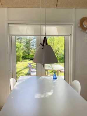 Un comedor con una mesa blanca, un florero azul y una lámpara colgante.
