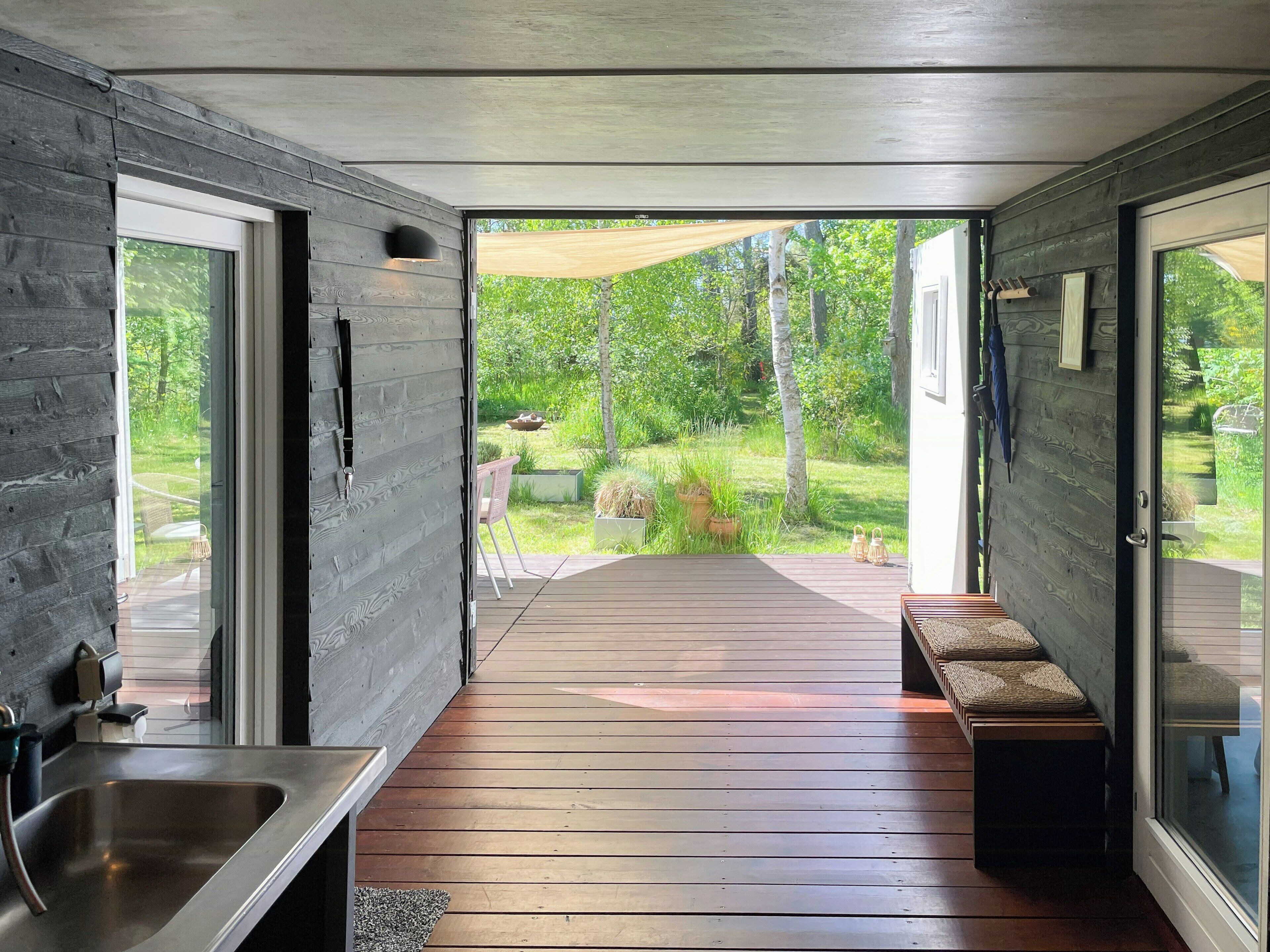 A modern kitchen with a built-in sink, wooden deck, and a view of a lush garden.