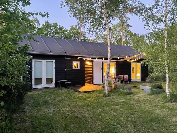 Una casa moderna con fachada oscura, puerta de vidrio y un patio con mobiliario exterior.