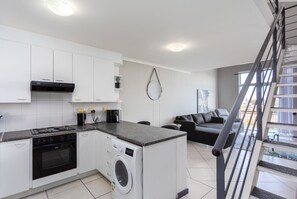 Eine moderne Küche mit Herd, Backofen und Waschmaschine, ein Wohnbereich mit Sofa und eine Treppe.
