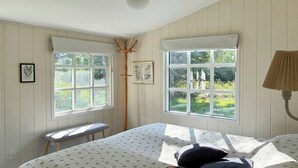 Un dormitorio con cama, dos ventanas, un banco y una lámpara.