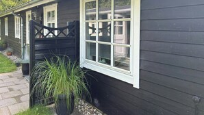 Un edificio de madera oscura con un marco blanco en la ventana, una reja negra y una planta en maceta.