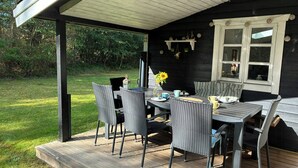 Un patio techado con una mesa y sillas, una ventana con cortinas y vistas al exterior.