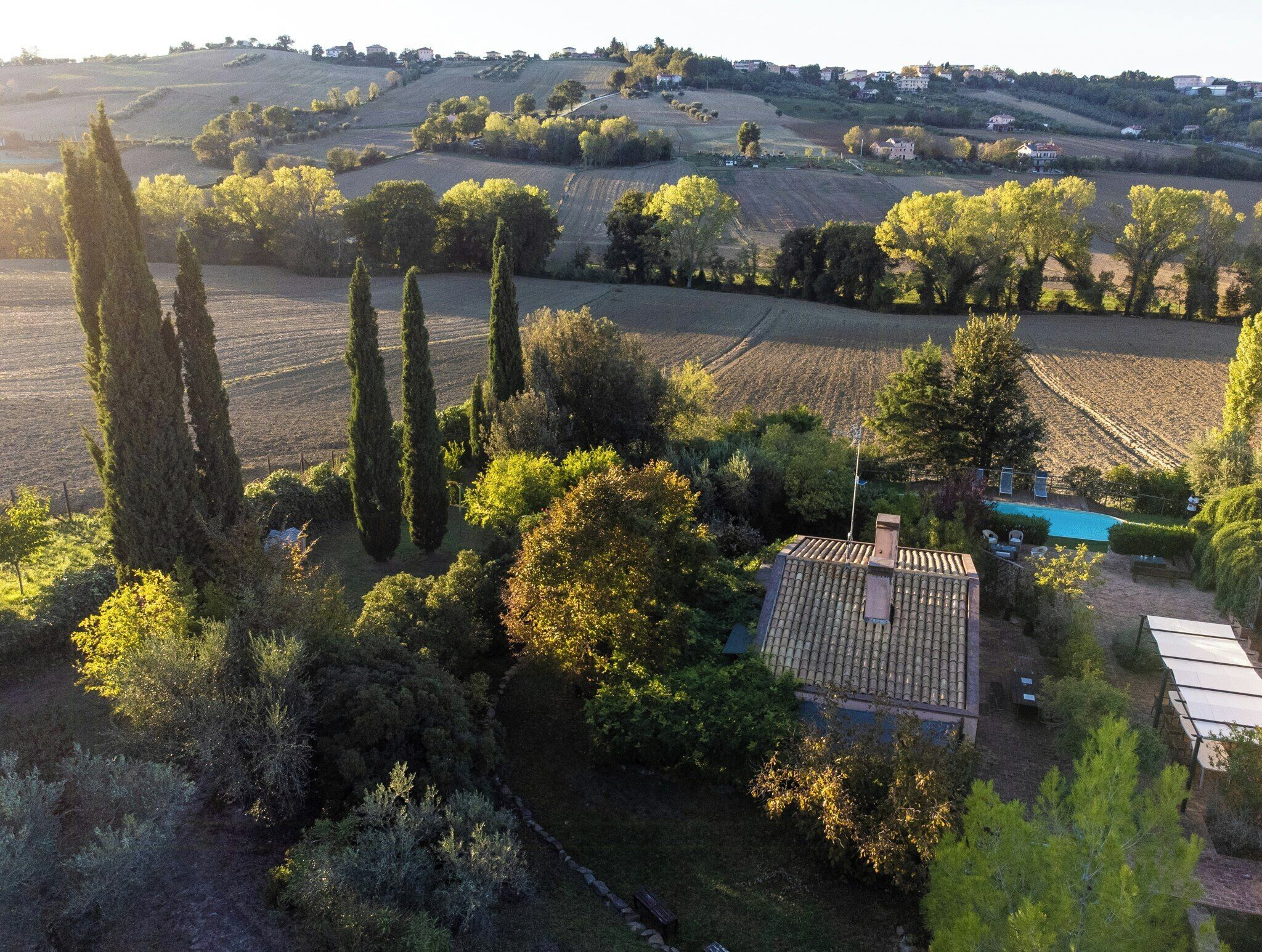 A rural landscape with rolling hills, a swimming pool, and a house with a tiled roof.