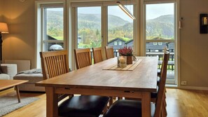Een eetgedeelte met een houten tafel en stoelen, een kaarsdecoratie en een uitzicht op een bergachtig landschap door grote ramen.
