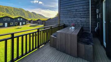 Eine Holzterrasse mit einer Bank, einem kleinen Tisch mit Topfpflanzen und Blick auf eine grüne Landschaft mit Gebäuden im Hintergrund.