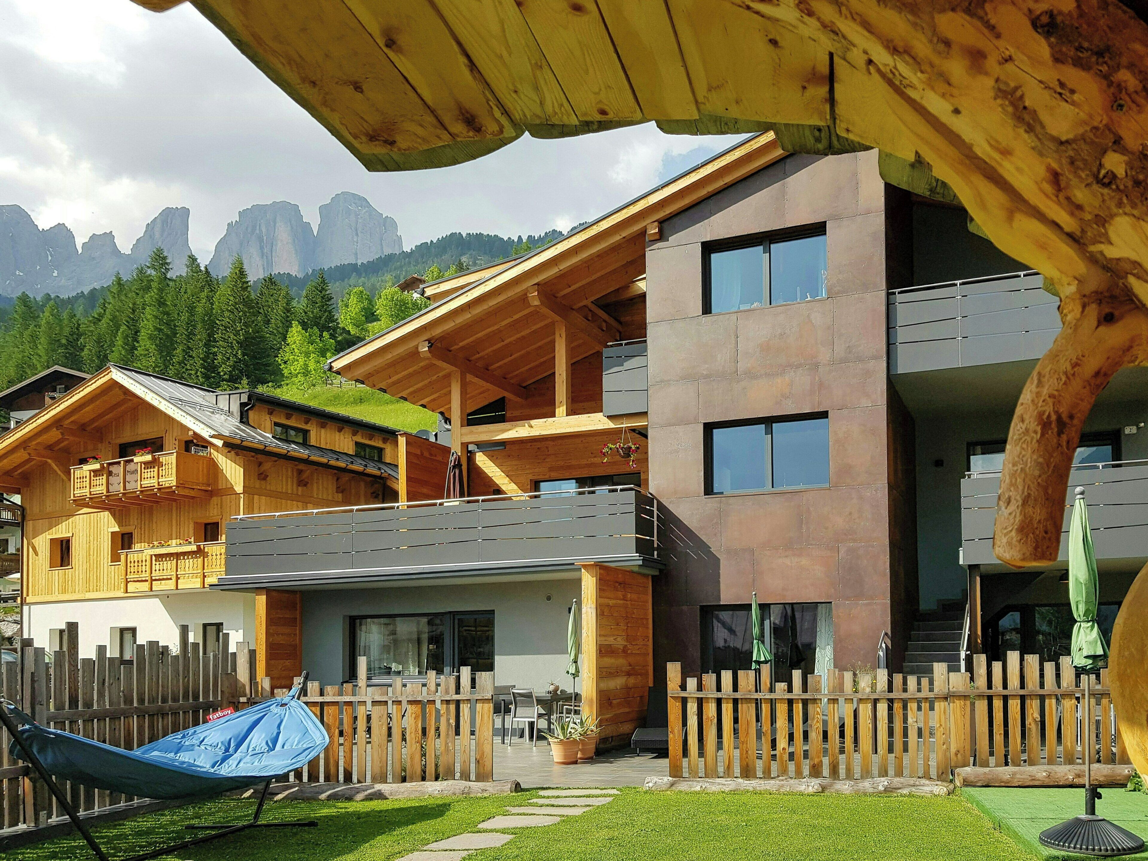 A modern building with a wooden balcony, a fenced patio area, and a view of mountains.