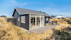 Ein Küstenhaus mit einer großen Glasveranda, einer Holzterrasse und blauem Himmel.
