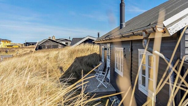 Ein Holzhaus mit Schornstein, einer Veranda mit Stühlen und einer Rasenfläche.