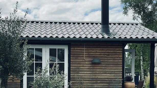 Eine Holzhütte mit einem Ziegeldach, einem Schornstein und einer Terrasse mit Blumentöpfen und Gartenmöbeln.