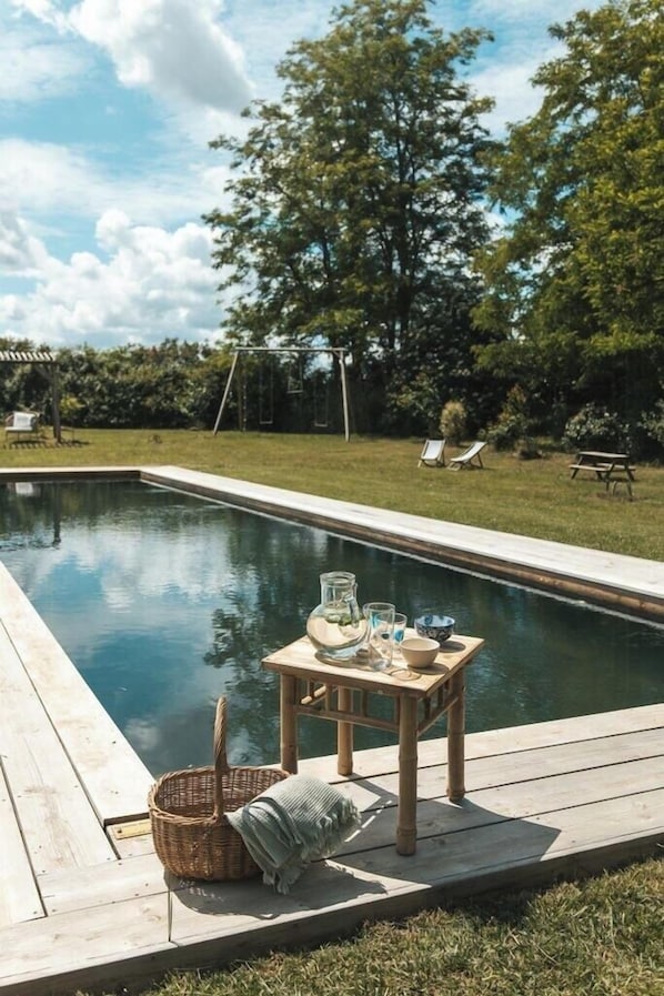 Ein Schwimmbecken mit Holzterrasse, ein kleiner Tisch mit Gläsern und einer Schüssel sowie ein Korb.