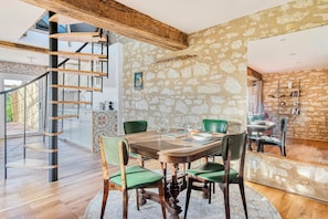 Ein Essbereich mit Holztisch, grünen Stühlen, einer Wendeltreppe und Steinwänden.