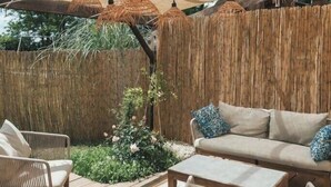 An outdoor seating area with a wooden deck, wicker furniture, and a canopy providing shade. - Eco-cottage with bird sanctuary in Anjou (Brissac Loire Aubance)