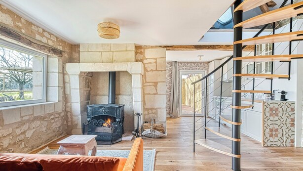 A spacious living area with a stone fireplace, a wooden staircase, and a view of the outdoors. - Eco-cottage with bird sanctuary in Anjou (Brissac Loire Aubance)