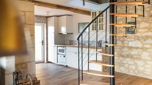 A kitchen with white cabinets, a wooden staircase, and a stone wall. - Eco-cottage with bird sanctuary in Anjou (Brissac Loire Aubance)