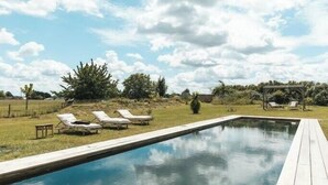 A rectangular swimming pool with a wooden deck, surrounded by lounge chairs and a pergola. - Eco-cottage with bird sanctuary in Anjou (Brissac Loire Aubance)