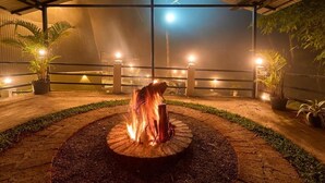 Un pozo de fuego en un diseño circular de ladrillo, rodeado por un camino empedrado, bajo una zona cubierta con techo de metal.