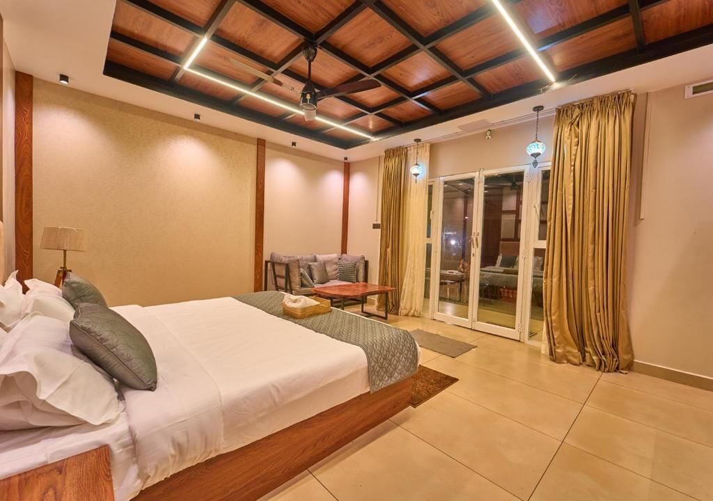 Habitación de hotel con cama, una mesita, una silla y un ventanal corredero que da a un espacio exterior.