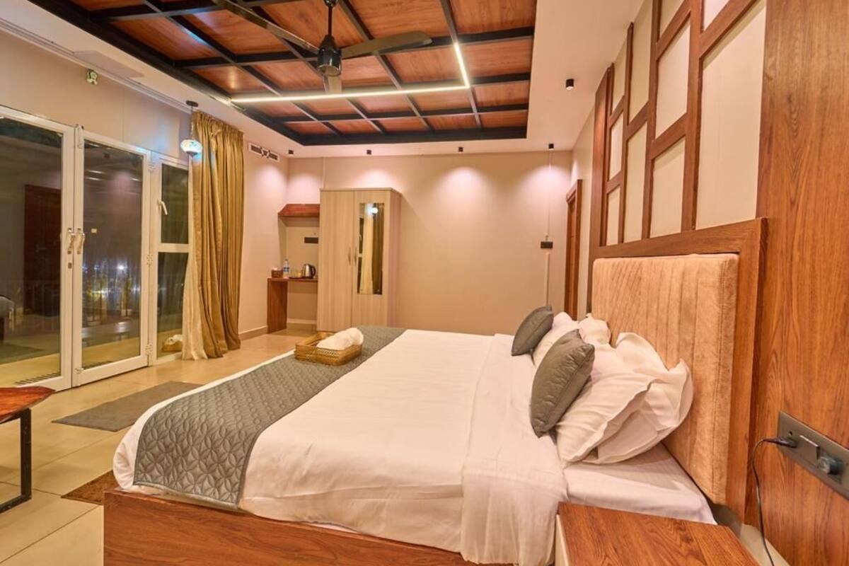 Habitación de hotel con una cama grande, cabecera de madera, ventilador de techo y puerta corrediza de vidrio que da a un área exterior.