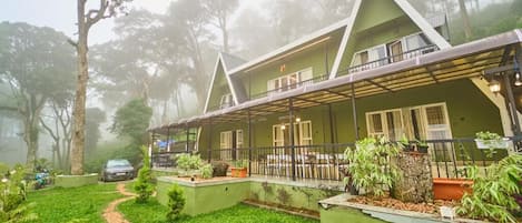 A green-roofed building with a covered outdoor area, surrounded by greenery and trees.