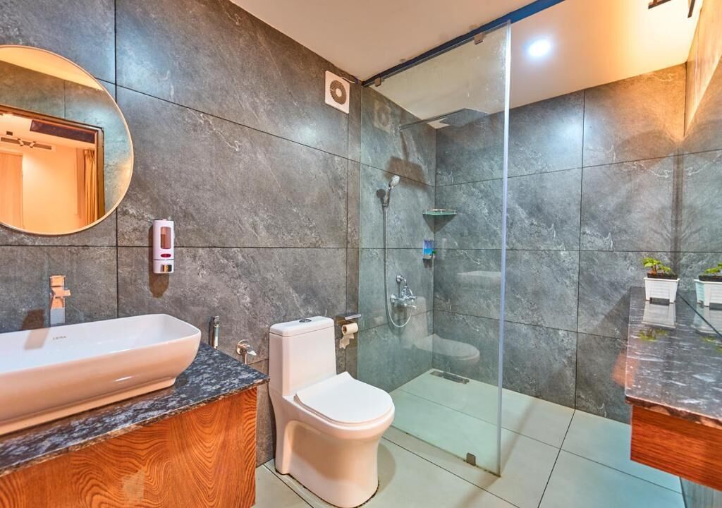 A modern bathroom with a glass shower enclosure, a white toilet, and a large sink with a wooden vanity.