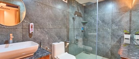 Un baño moderno con cabina de ducha de vidrio, inodoro blanco y lavamanos grande con mueble de madera.