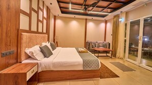 Un dormitorio con cabecera de madera, cama con ropa blanca, mesita de noche, escritorio, silla y puerta corrediza de vidrio al exterior.