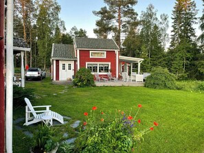 A red house with a porch, a car parked outside, and a garden with red flowers. - 18th-century timber house by sea bay near Umeå (Täfteå)