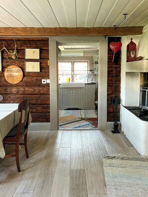 A wooden interior with a dining area, kitchen, and a view into the adjacent room. - 18th-century timber house by sea bay near Umeå (Täfteå)