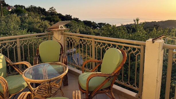 Un balcone con mobili in vimini, un tavolino in vetro e vista mare.