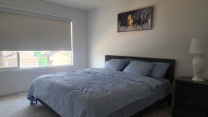 Una camera da letto con un letto, un comodino, una lampada, una finestra con persiane e un quadro appeso al muro.