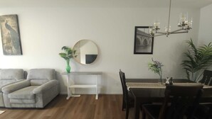 Un soggiorno con un divano, un tavolo da pranzo con sedie, un lampadario, uno specchio e una pianta.