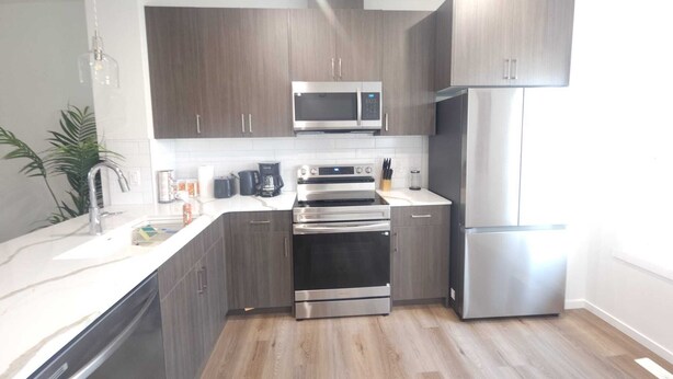 Una cucina moderna con pensili in legno scuro, elettrodomestici in acciaio inossidabile e un piano di lavoro bianco.